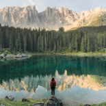 One person, looking very small gazing at the reflection of mountains in a lake.