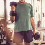 A Man in a green t-shirt lifting hand weights at the gym.