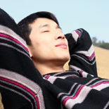 Young Asian man leaning back into his arms in the sun with his eyes closed.