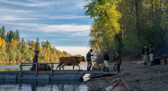 travelers guiding a cow across a bridge in First Cow