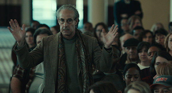 Stanley Tucci as Charles Wolf at the town hall meeting with victims and families