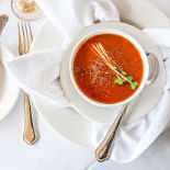 Tomato soup served in pretty white bowls with gold silverware.