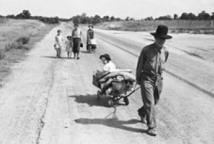 Migrant family walking on road, pulling belongings in carts and wagons. Pittsburg County, Oklahoma. June 1938. Credits: Dorothea Lange
